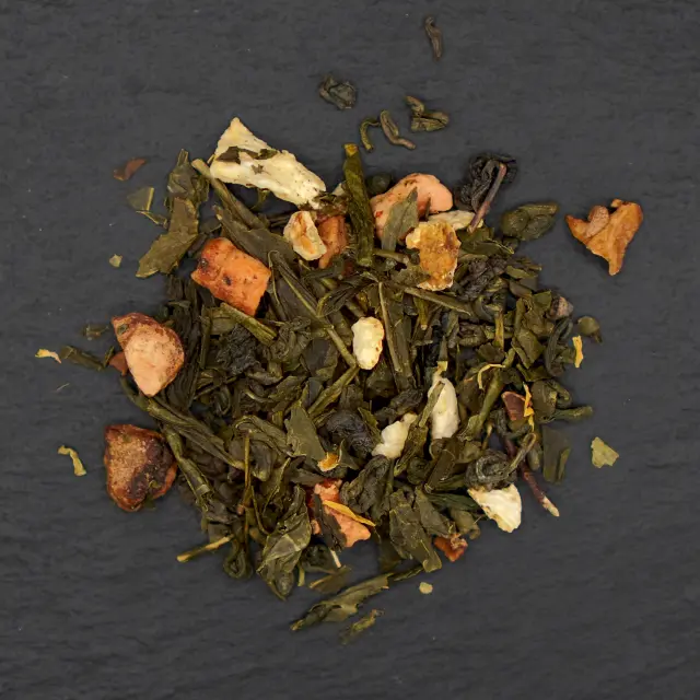 Un morman de ceai verde Sencha Mandarin, cu frunze uscate de ceai, bucăți de fructe confiate și coji de citrice, pe o suprafață închisă la culoare.