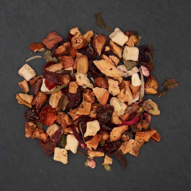 Un amestec de ceai de fructe uscate, cu bucăți de măr, fructe de pădure roșii închise și alte fructe, pe un fundal gri închis.